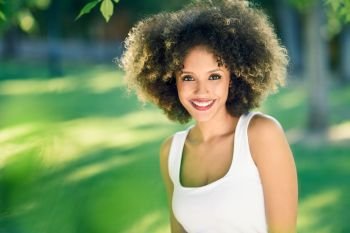 Young black woman with afro hairstyle smiling in urban park. Mixed girl wearing casual clothes.