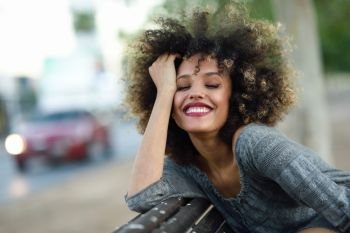 Young black woman with afro hairstyle smiling in urban background. Mixed girl wearing casual clothes.