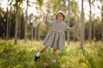 Little girl walking in nature field wearing beautiful dress