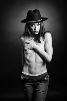 Topless woman wearing blue jeans, panties and hat on black background