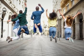 Multi-ethnic group of young people having fun together outdoors in urban background. group of people jumping together. Rear view.