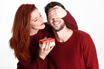 Young woman giving a gift to his man. Beautiful couple dressed in red on white background. Redhead girl