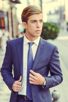 Portrait of an attractive young businessman in urban background wearing blue suit a necktie. Blonde hair