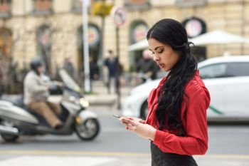 Portrait of hispanic bussinesswoman in urban background looking at her mobile phone