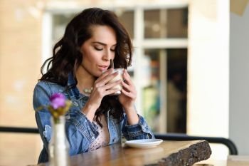 Young woman sitting indoor drinking coffee. Cool young modern caucasian female in her 20s. Cafe city lifestyle. 