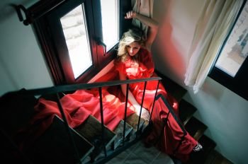 Portrait of a beautiful blonde woman sitting in stairs wearing a red dress