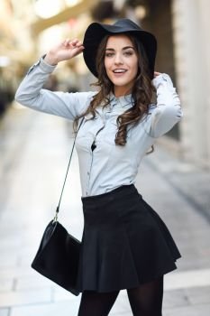 Portrait of young woman in urban background wearing casual clothes and hat 
carrying a bag