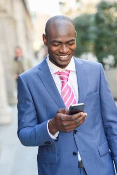 Portrait of a black businessman wearing suit reading his smart phone in urban background