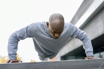 Fitness black man exercising push ups. Male model cross-training in urban background  African guy in his twenties doing workout outdoors in the street.