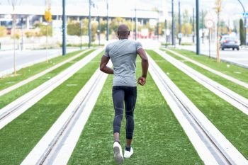Back view of black man running in urban background. Male doing workout outdoors.