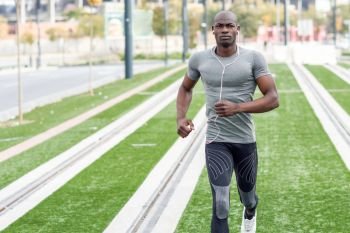 Black man running and listening to music in urban background. Handsome male doing workout outdoors.