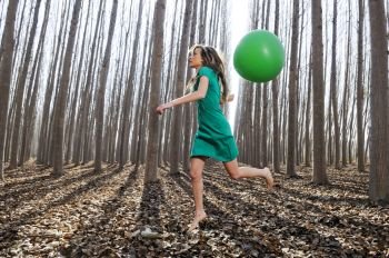 Beautiful blonde girl, dressed in green, jumping into the woods with a balloon in Fuente Vaqueros, Granada, Spain