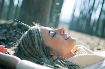Smiling blonde girl lying on leaves in a forest of poplars