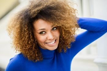 Close-up portrait of beautiful young African American woman, model of fashion, smiling with afro hairstyle and green eyes wearing blue sweater in urban background