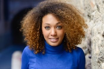 Close-up portrait of beautiful young African American woman with afro hairstyle and green eyes wearing blue sweater. Girl smiling.