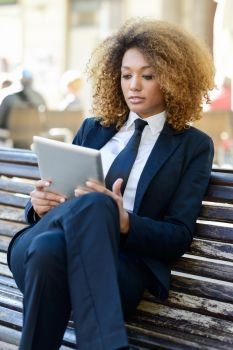 Beautiful black curly hair african woman using tablet computer in town. Businesswoman wearing suit with trousers and tie