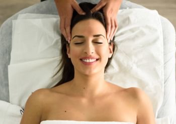 Top view of young caucasian smiling woman receiving a head massage in a spa center with eyes closed. Female patient is receiving treatment by professional therapist.