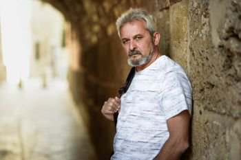 Portrait of a mature serious man in urban background. Senior male with white hair and beard wearing casual clothes.