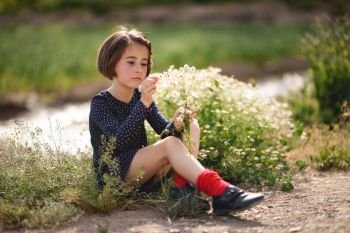 Little girl sitting in nature field wearing beautiful dress with flowers in her hand.