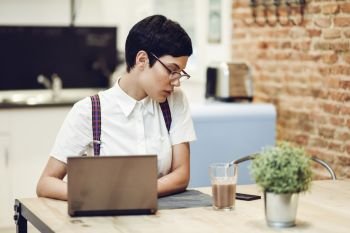 Spain, Madrid, Madrid. Young woman with very short haircut and eyeglasses typing with a laptop at home. Working at home concept.