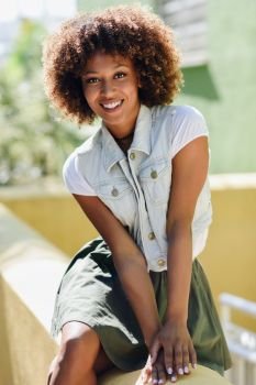 Young black woman, afro hairstyle, smiling. Girl, model of fashion, wearing casual clothes in urban background. Female with skirt and denim vest.