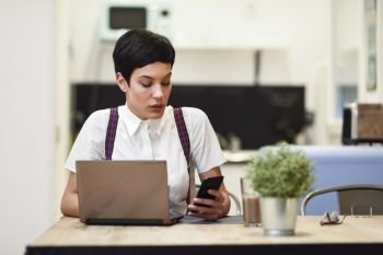 Young woman with very short haircut looking at her smart phone. Businesswoman working at home concept.