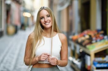 Smiling young woman in urban background. Blond girl wearing with nice hair casual clothes in the street. Straight hairstyle.