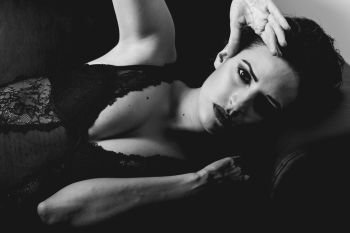 Young brunette woman looking at camera laying on a couch. Attractive girl, model of fashion in black lingerie. Black and white photograph.