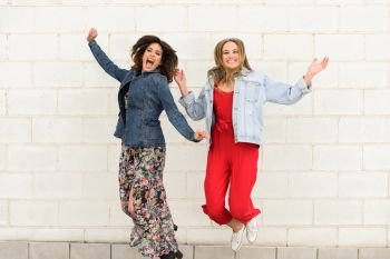 Two young happy women jumping in urban background. Funny friends. Lifestyle concept.