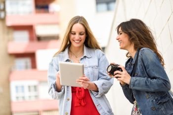 Two young tourist women looking maps with digital tablet outdoors. Travelers concept.