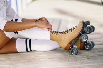 Close-up of black girl sitting on wooden floor puts on skates outdoors. Unrecognizable woman. Rollerblading concept