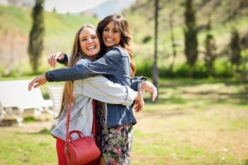 Two happy girls hugging in urban park. Blonde and brunette girls wearing casual clothes outdoors.