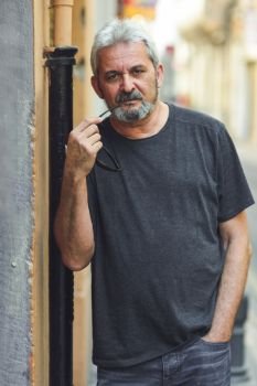 Mature man with grey hair standing in urban background. Mature man looking at camera in urban background. Senior male with white hair and beard wearing casual clothes.