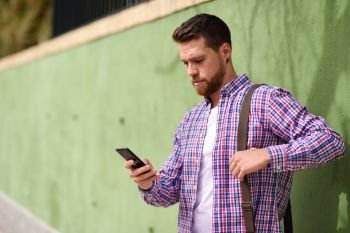 Young man looking his smart phone in urban background. Lifestyle. Young man looking his smart phone in urban background. Guy wearing casual clothes. Lifestyle concept.