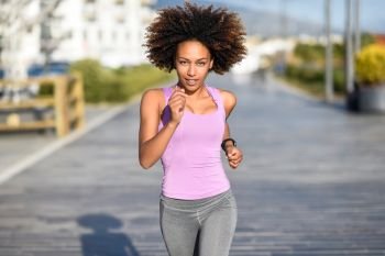 Black woman, afro hairstyle, running outdoors in urban road. . Black woman, afro hairstyle, running outdoors in urban road. Young female exercising in sport clothes.