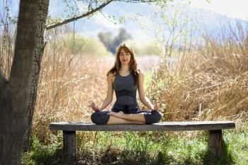 Young beautiful woman doing yoga in nature. Young woman doing yoga in nature. Female wearing sport clothes in lotus figure.