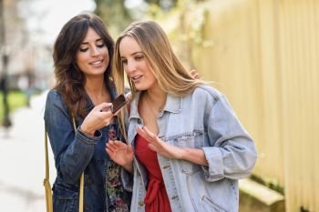 Two young women recording a voice message with smart phone. Two young women recording a voice message with smart phone outdoors. Girls using the voice recognition of the smartphone