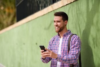 Young man laughing with his smart phone in urban background. Lif. Young man laughing with his smart phone in urban background. Guy wearing casual clothes. Lifestyle concept.