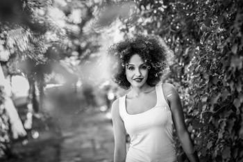 Young black woman with afro hairstyle smiling in urban park. Young black woman with afro hairstyle smiling in urban park. Mixed girl wearing casual clothes. Black and white photograph.