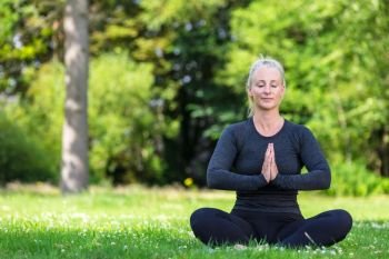 Mature middle aged fit healthy woman practicing yoga outsidein a natural tranquil green environment
