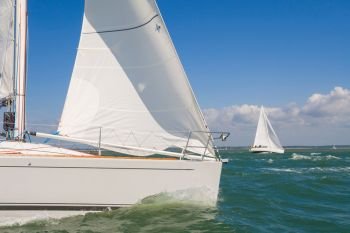 Two beautiful white yachts or sail boats sailing or racing at sea on a bright sunny day
