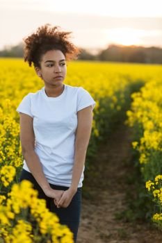 Beautiful mixed race African American girl teenager female young woman outside on a path in a field of yellow flowers looking scared sad depressed or thoughtful