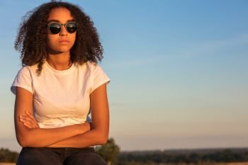 Beautiful mixed race African American girl teenager female young woman outside wearing sunglasses looking sad depressed or thoughtful at sunrise or sunset