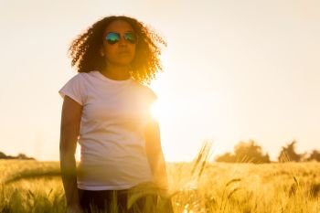 Beautiful happy mixed race African American female girl teenager young woman wearing relective aviator sunglasses in a cornfield at golden sunset or sunrise