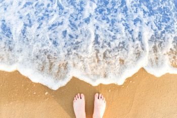 Woman’s feet on yellow beach sand with sea wave and white foam. Woman’s feet on yellow beach sand