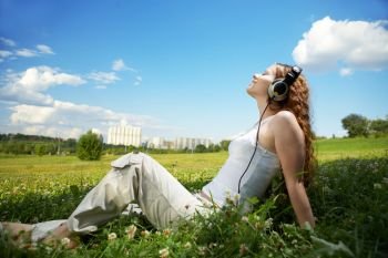 The girl with headphones against park and the sky. Enjoy music!