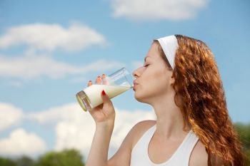 The woman drinks milk against the blue sky. Healthy product