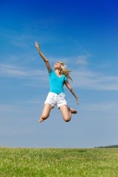 The happy woman jumps in a summer green field against the blue sky