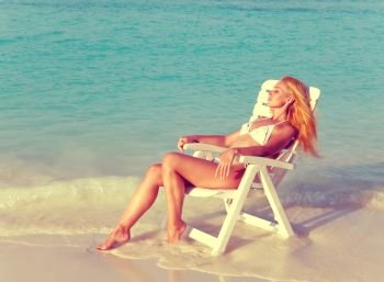 Young pretty woman tans in beach chair, it put in ocean,with a retro effect