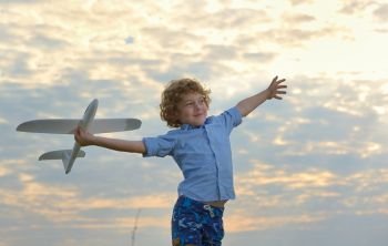 little boy holding a wooden airplane model on field